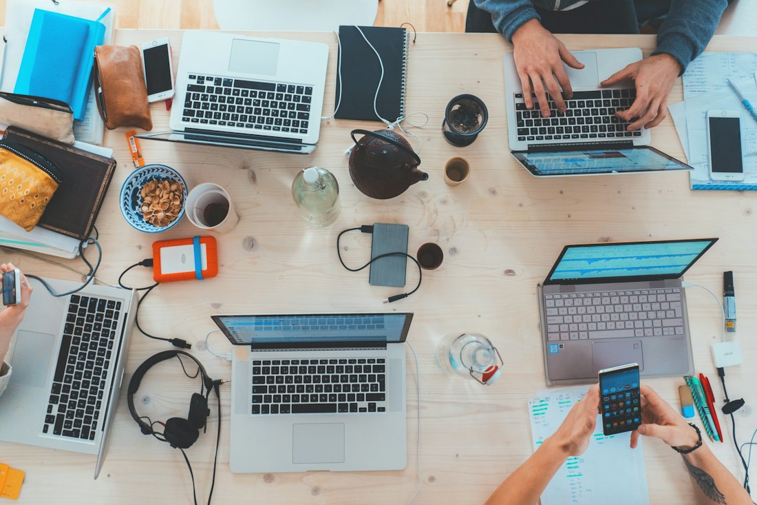 Vista de cima de uma mesa com várias pessoas trabalhando em notebooks