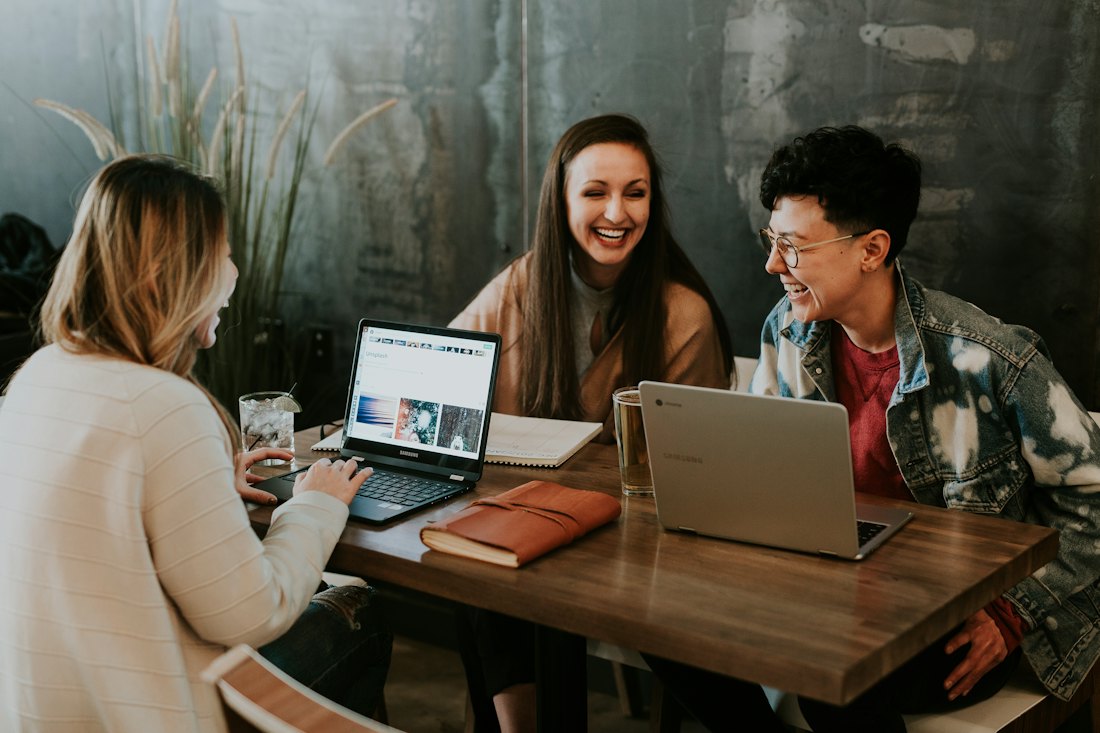 Pessoas conversando em volta de notebooks em uma mesa de madeira